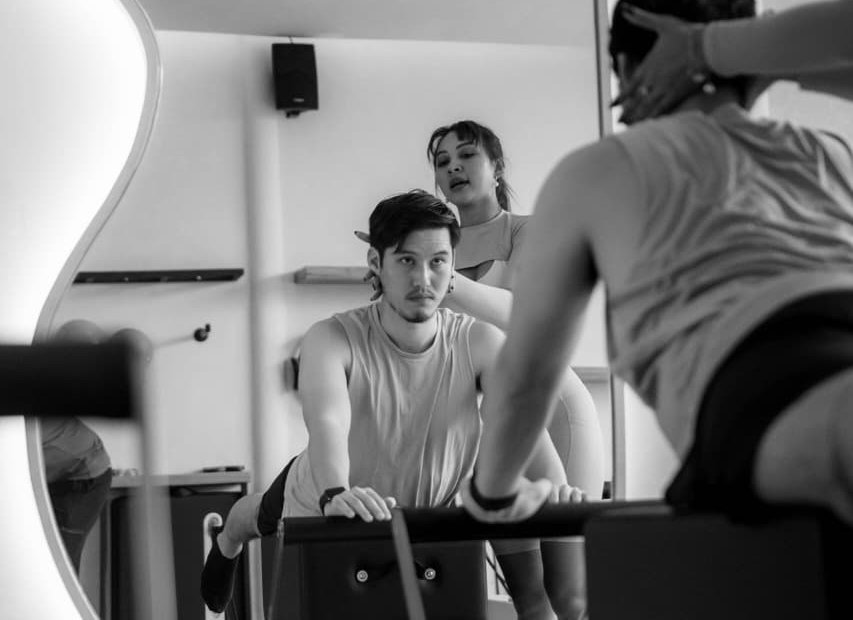 Nana coaching a client on the reformer, seen in the studio mirror